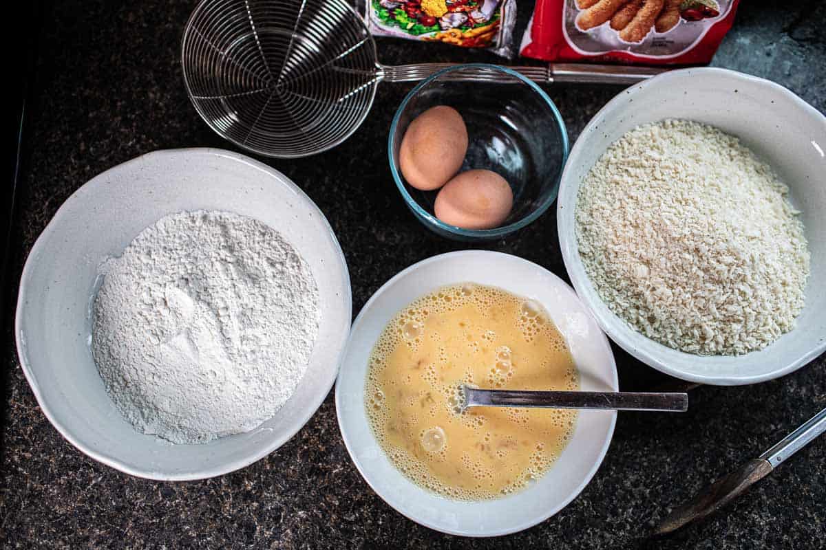 bowls of flour, eggs and bread crumb and eggs on the counter. 