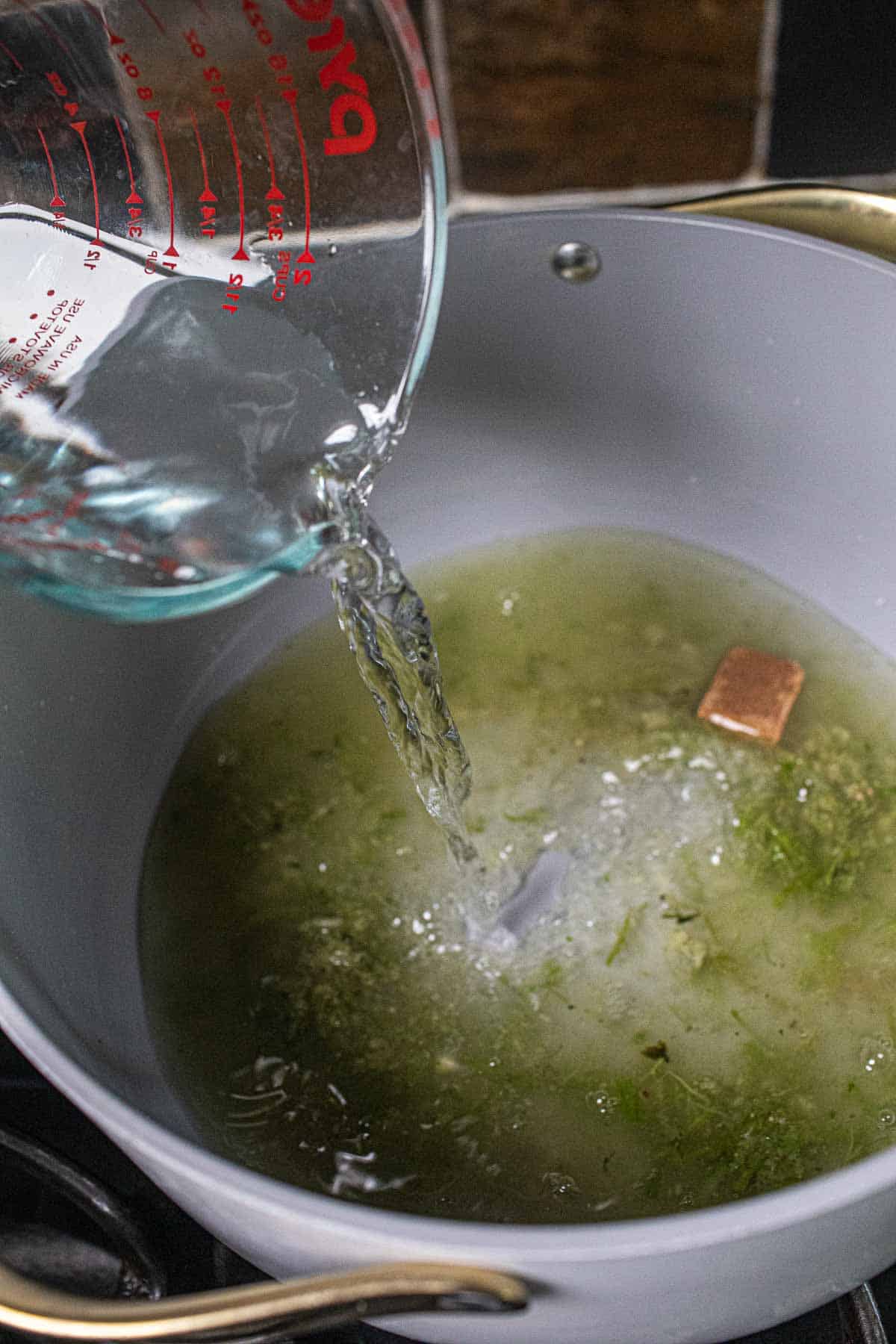 Pouring water into a pot with green paste for soup base. 