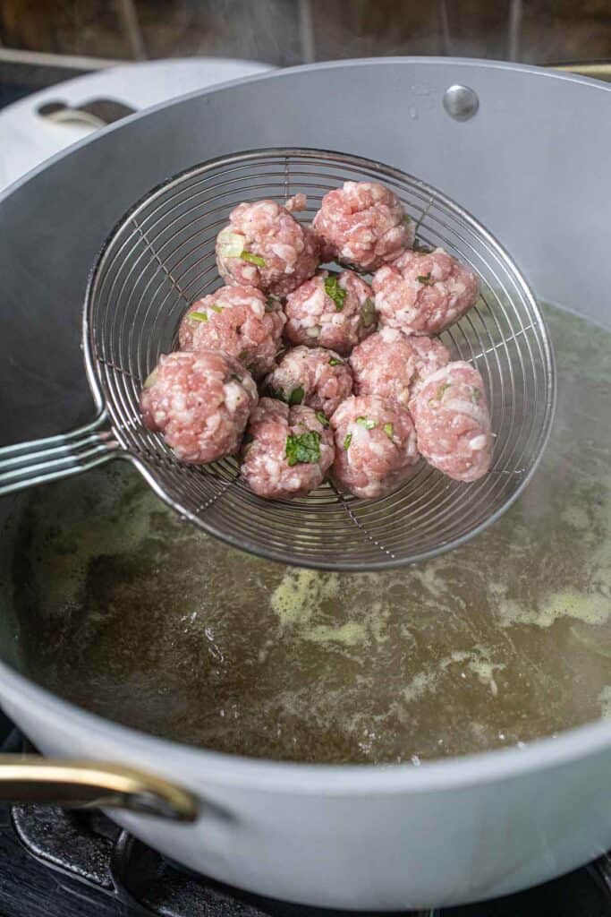 Pork meatballs in a strainer over a soup pot. 