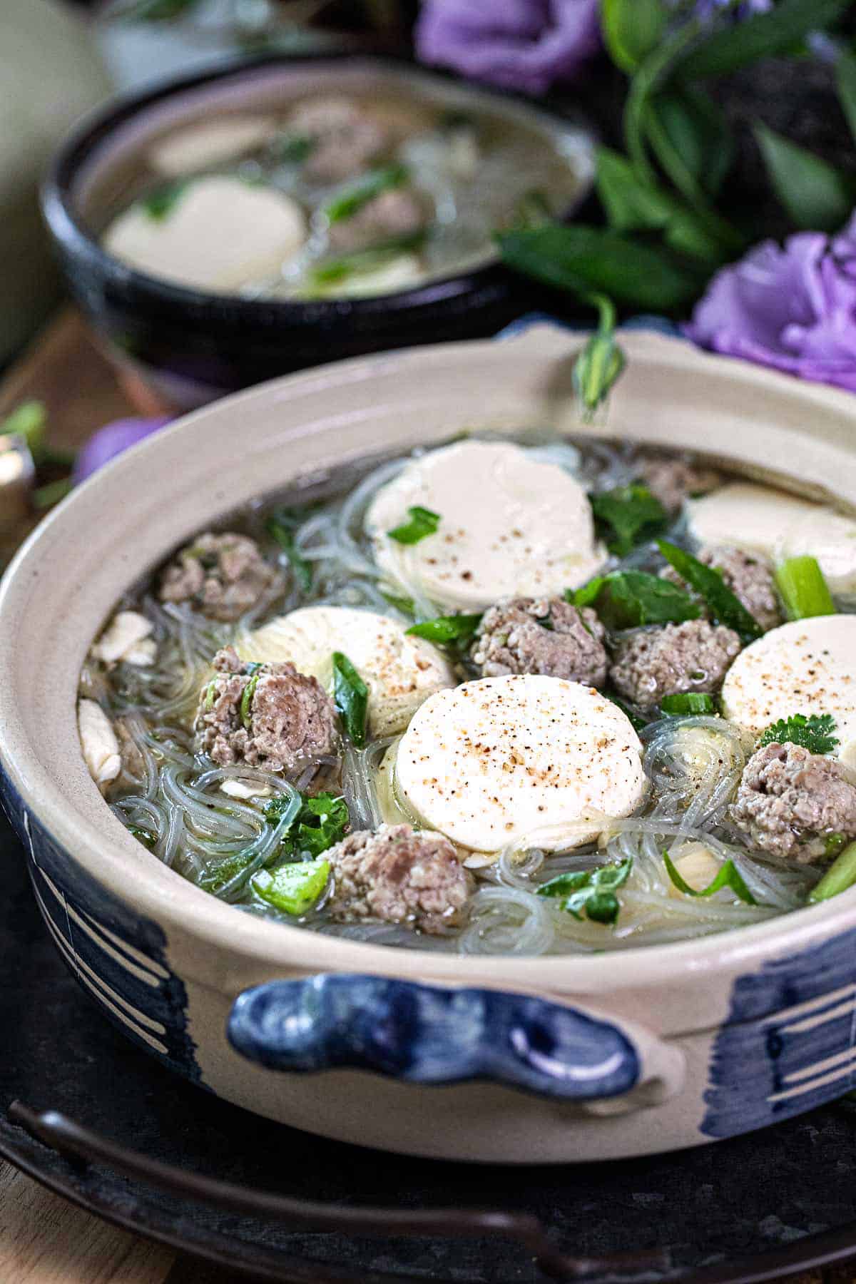 Glass Noodle soup in a bowl on the table with flowers around. 