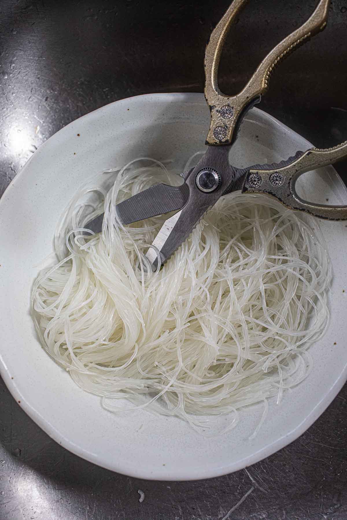 Scissor cutting glass noodles in a bowl. 