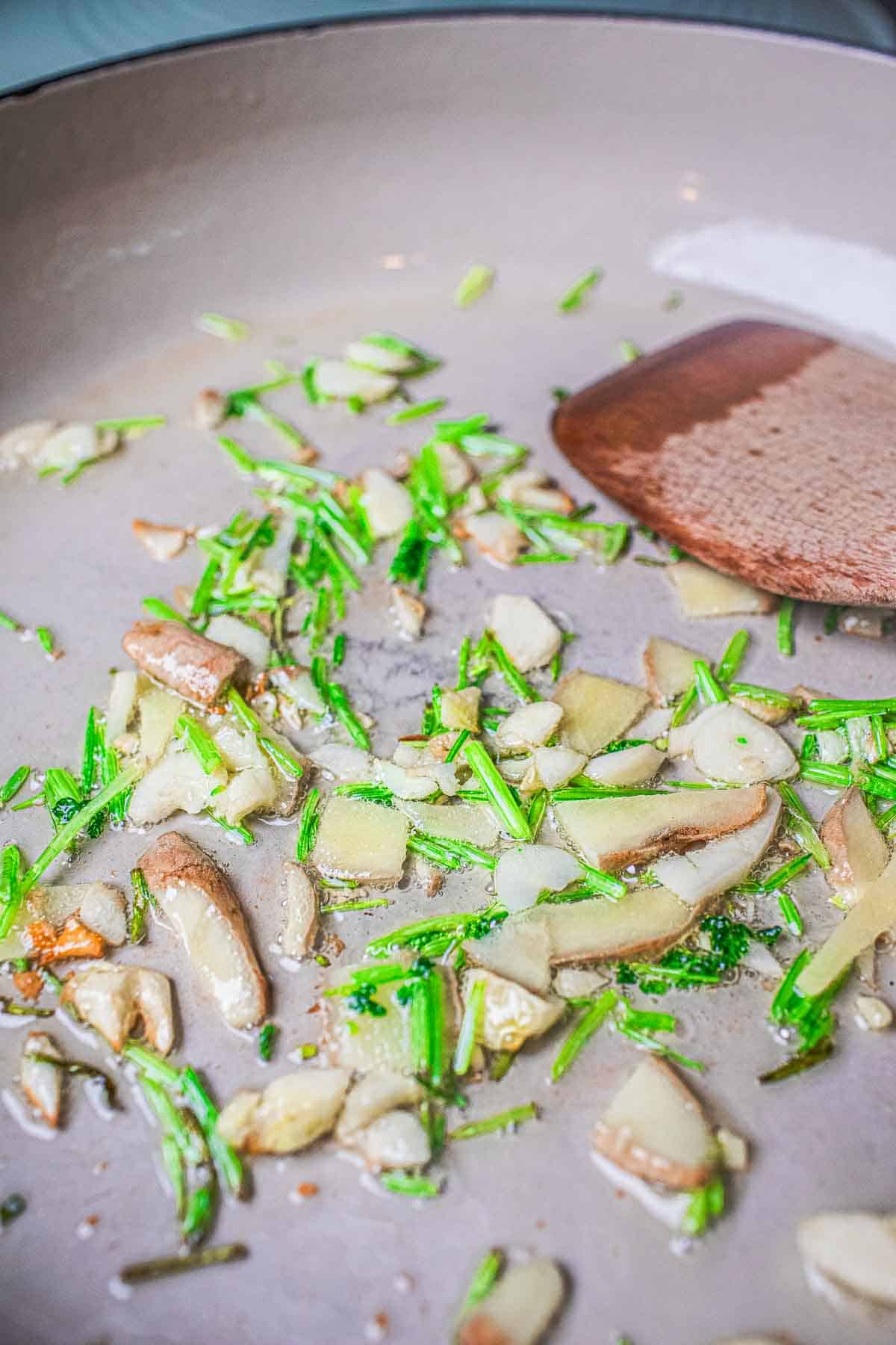 Garlic, ginger and cilantro stems frying in a skillet. 