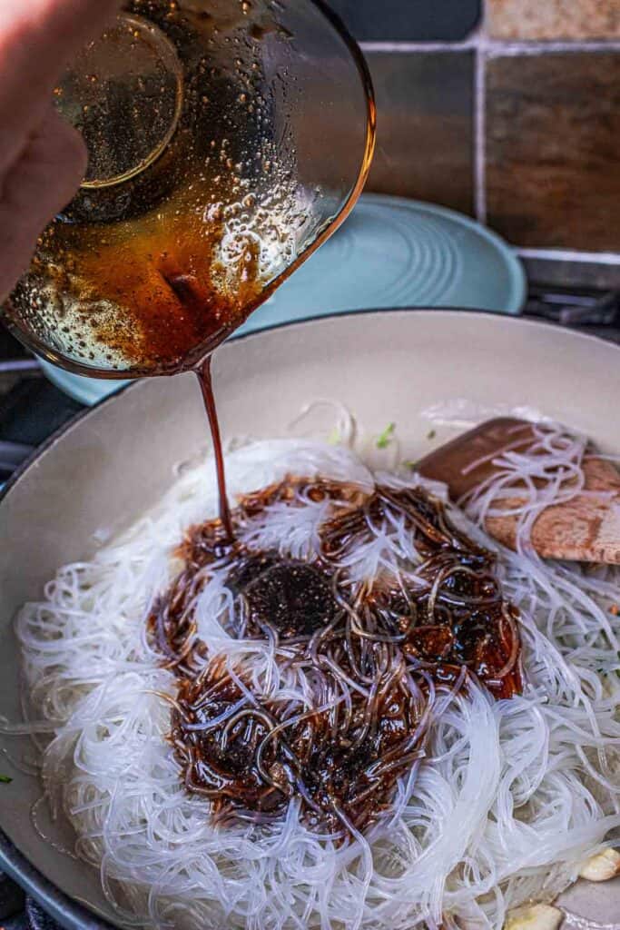 Soy sauces pouriong over glass noodle in a pan. 