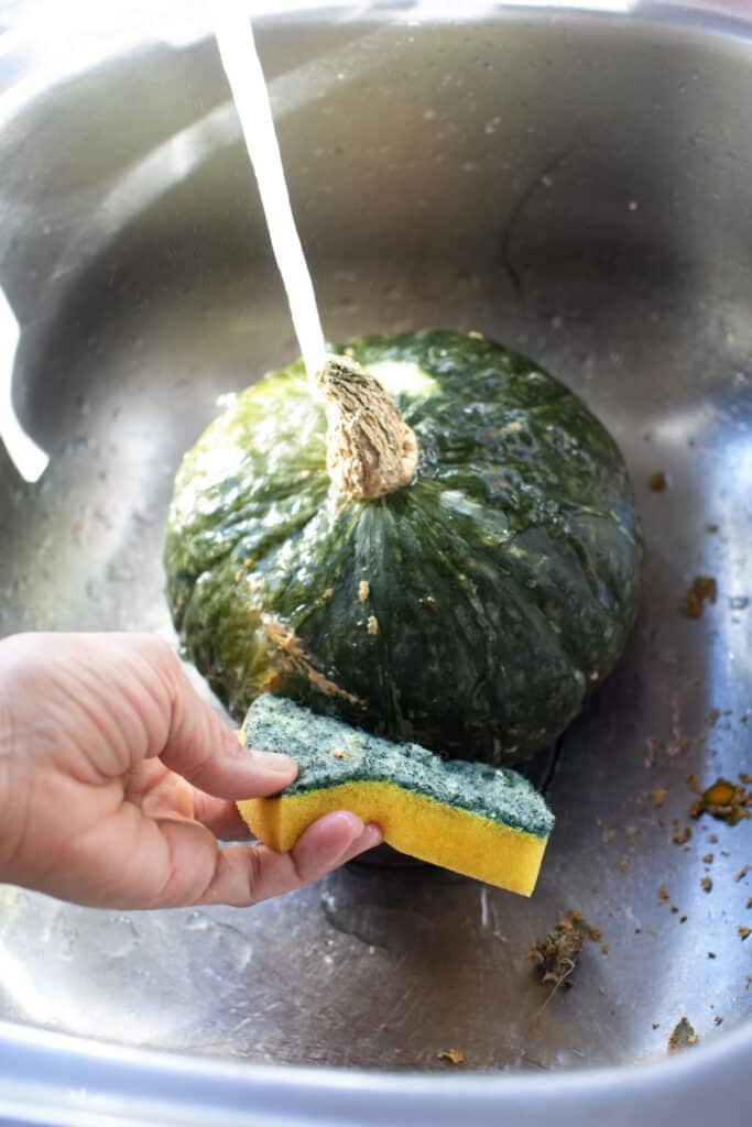 Faucet Water running over kabocha squash in a sink.