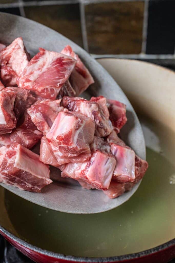 Pork ribs pouring into a pot of stock. 