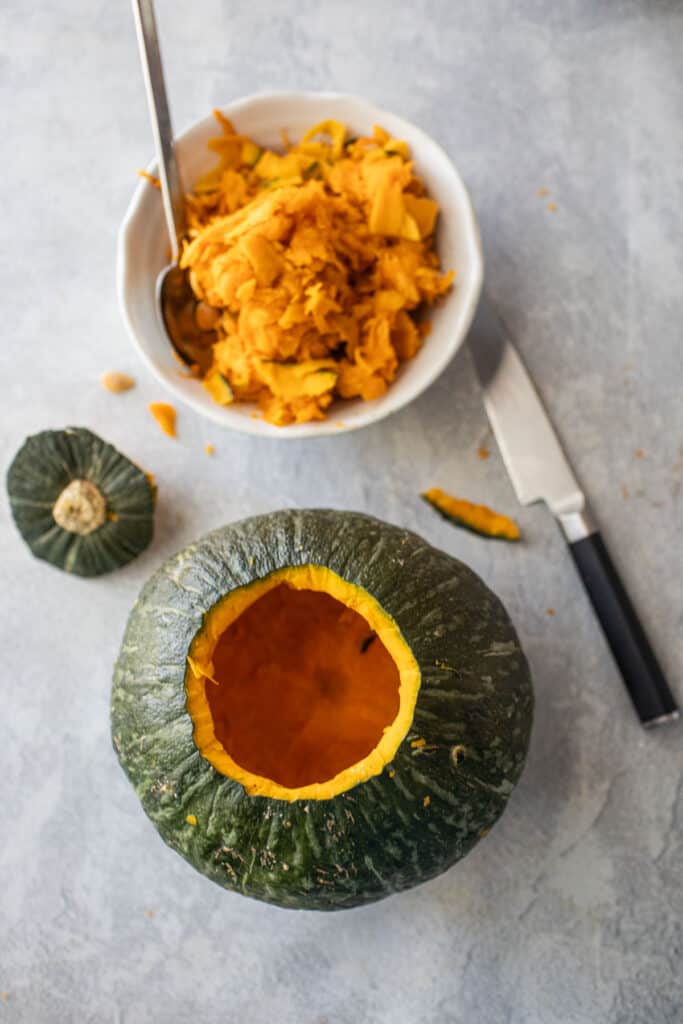 Carved hollow up green pumpkin next to a bowl of fibers and seeds.