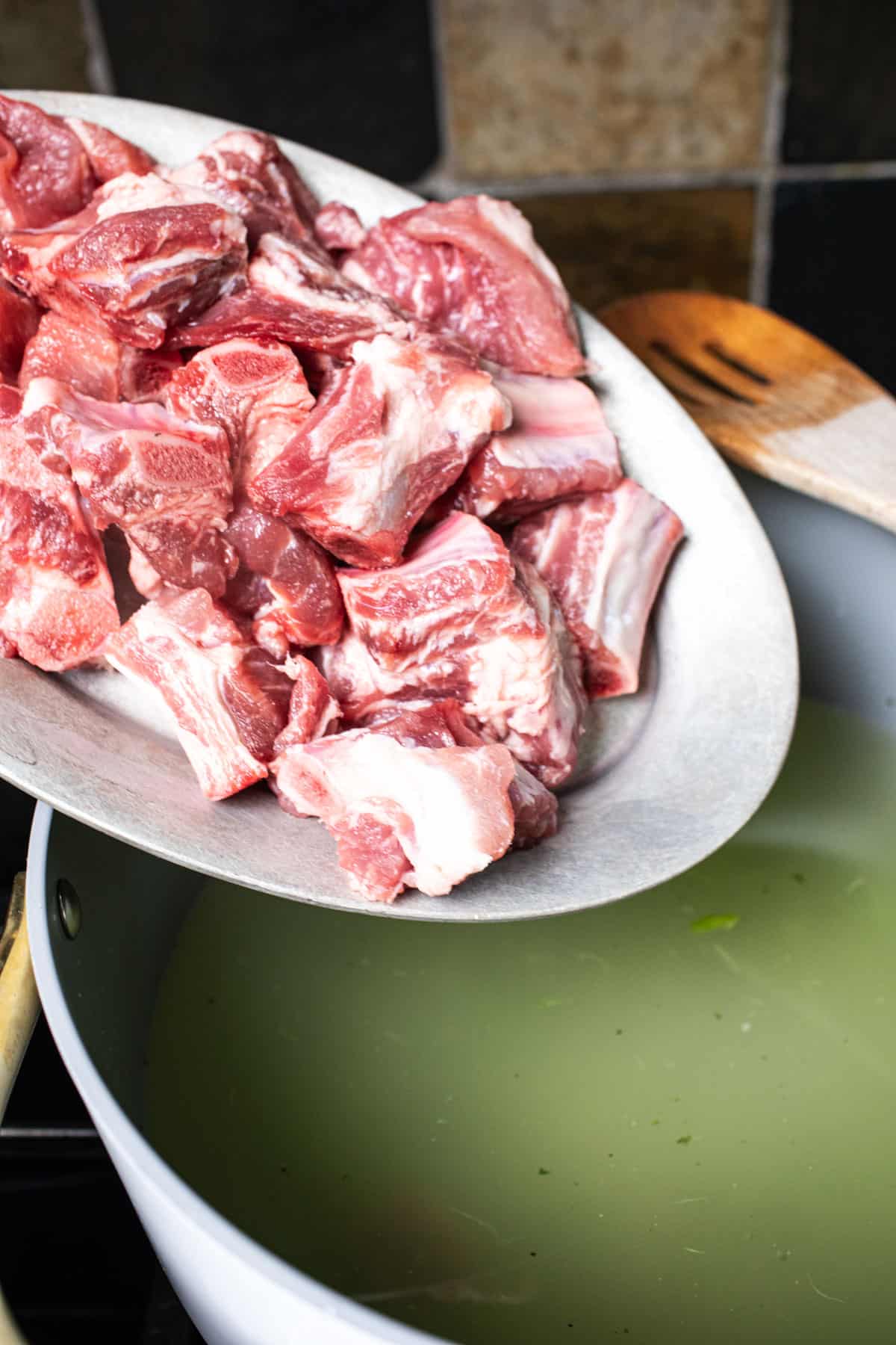 Pork ribs pouring into a soup pot wit. green broth. 