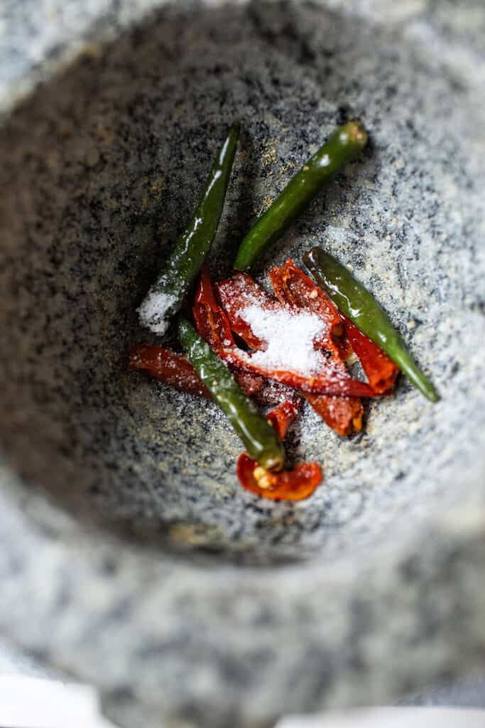 red and green chilis with salt in a mortar. 