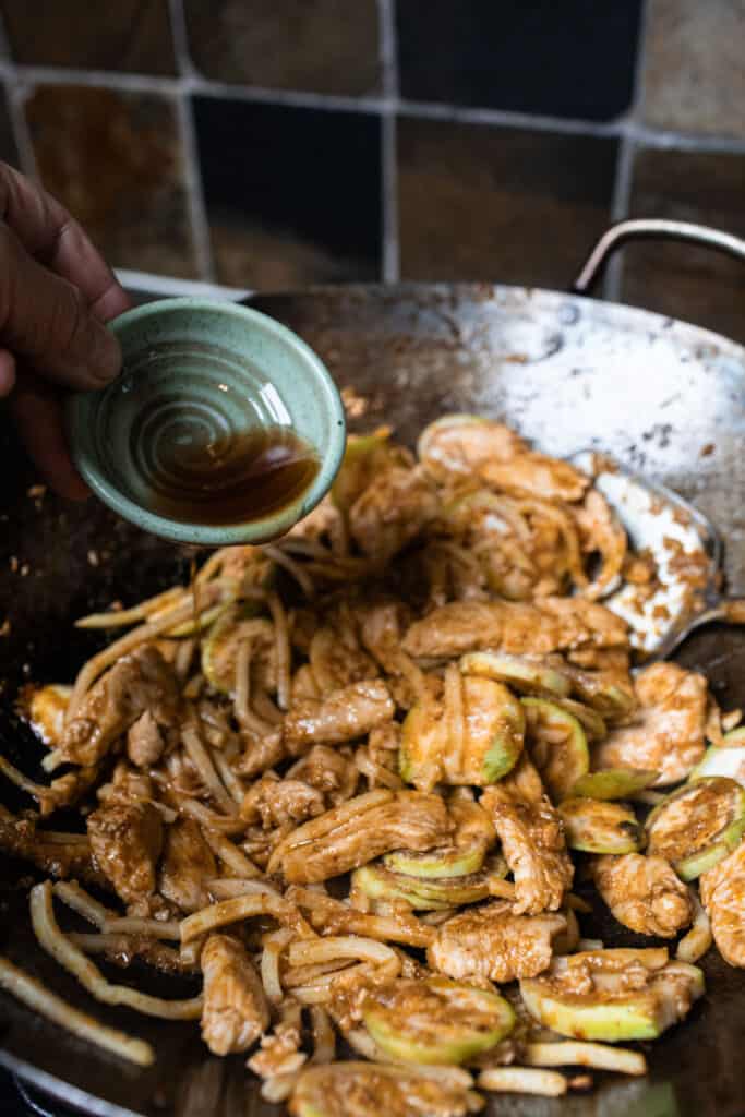 Sauce pouring into chicken in a wok. 