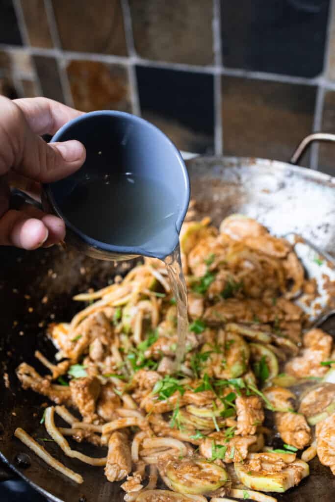 stock pouring into chicken in a wok. 