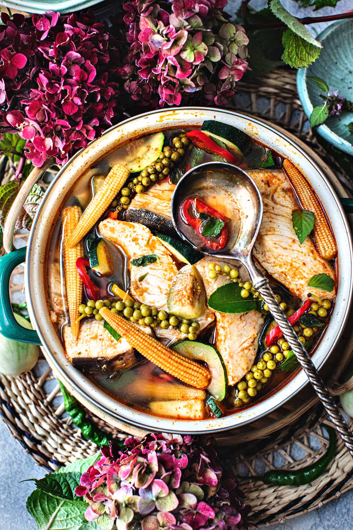 A spoon scooping Thai Jungle Curry with vegetables in a bowl on the table. 