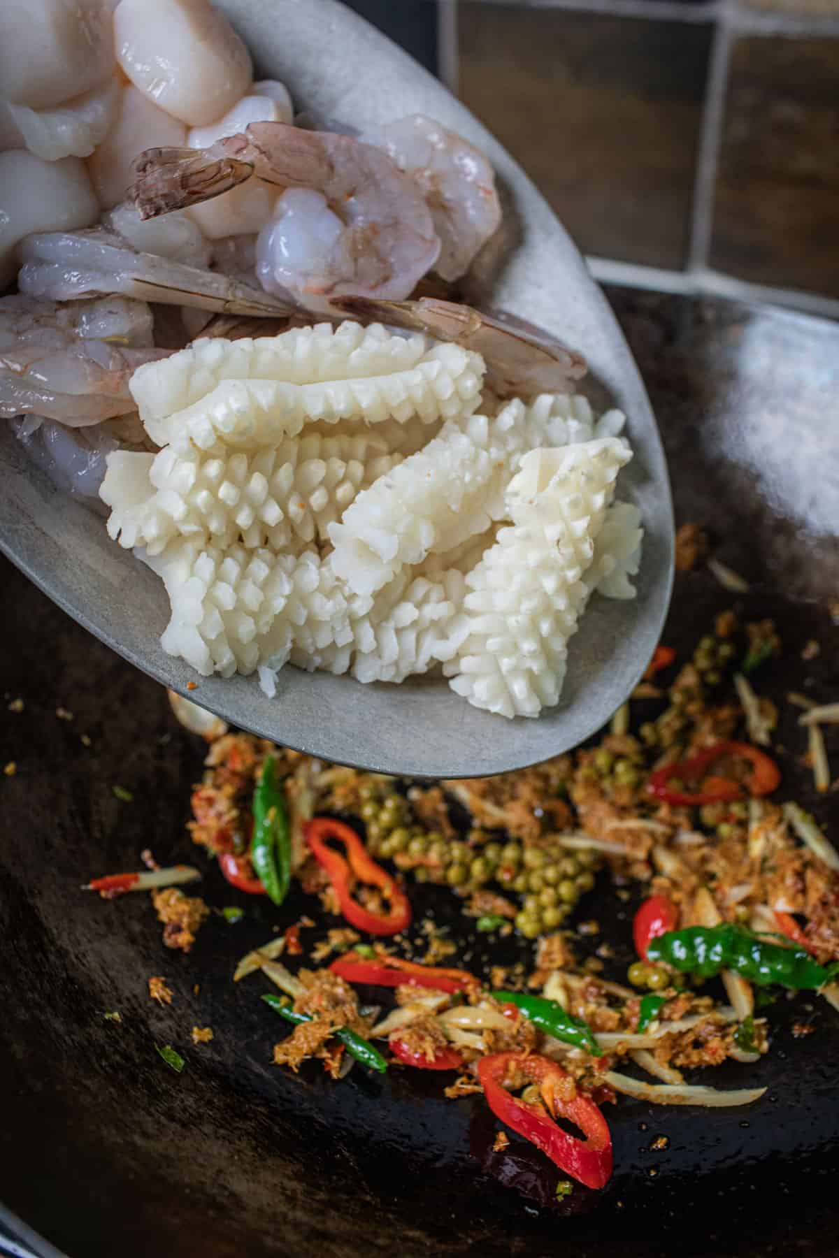 Seafood pouring into pad cha past in a wok. 