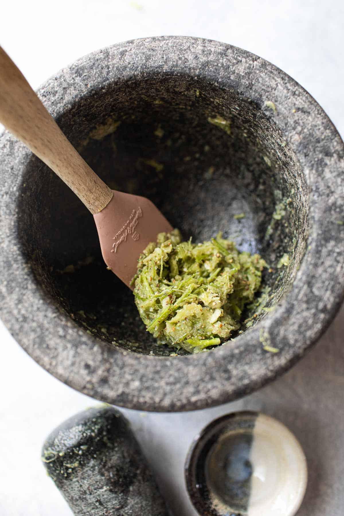 Spatula lifting green paste in a mortar. 