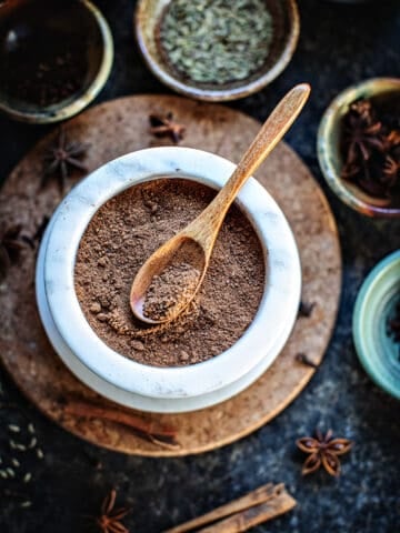 5 Spice powder in a white bowl with a spoon in the middle.