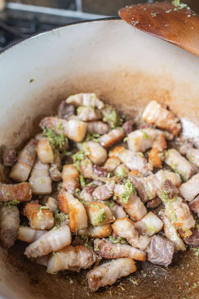 Thai pork belly frying in a pot with gree paste.