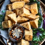 Tofu puffs on a platter with sauce on the side.