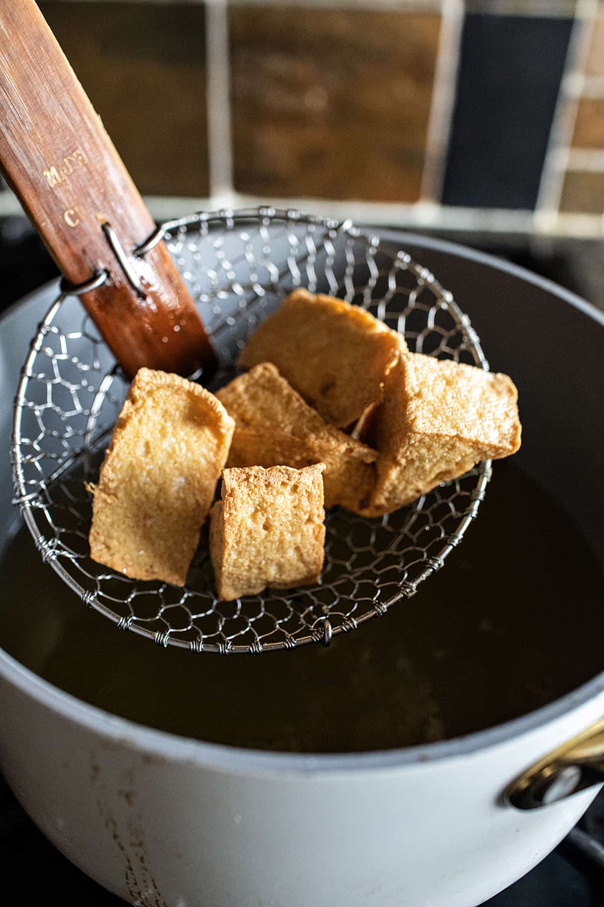 Slooted spoon lifting fried tofu puffs.