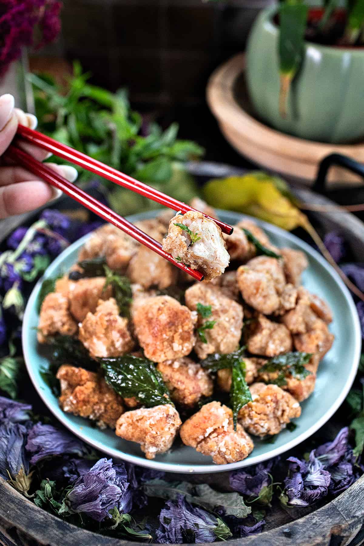 Chopsticks lifting a piece of Taiwanese popcorn chicken from a plate. 