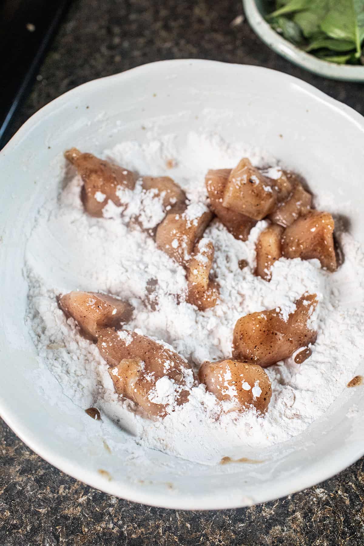 Chicken pieces in a bowl of flour. 