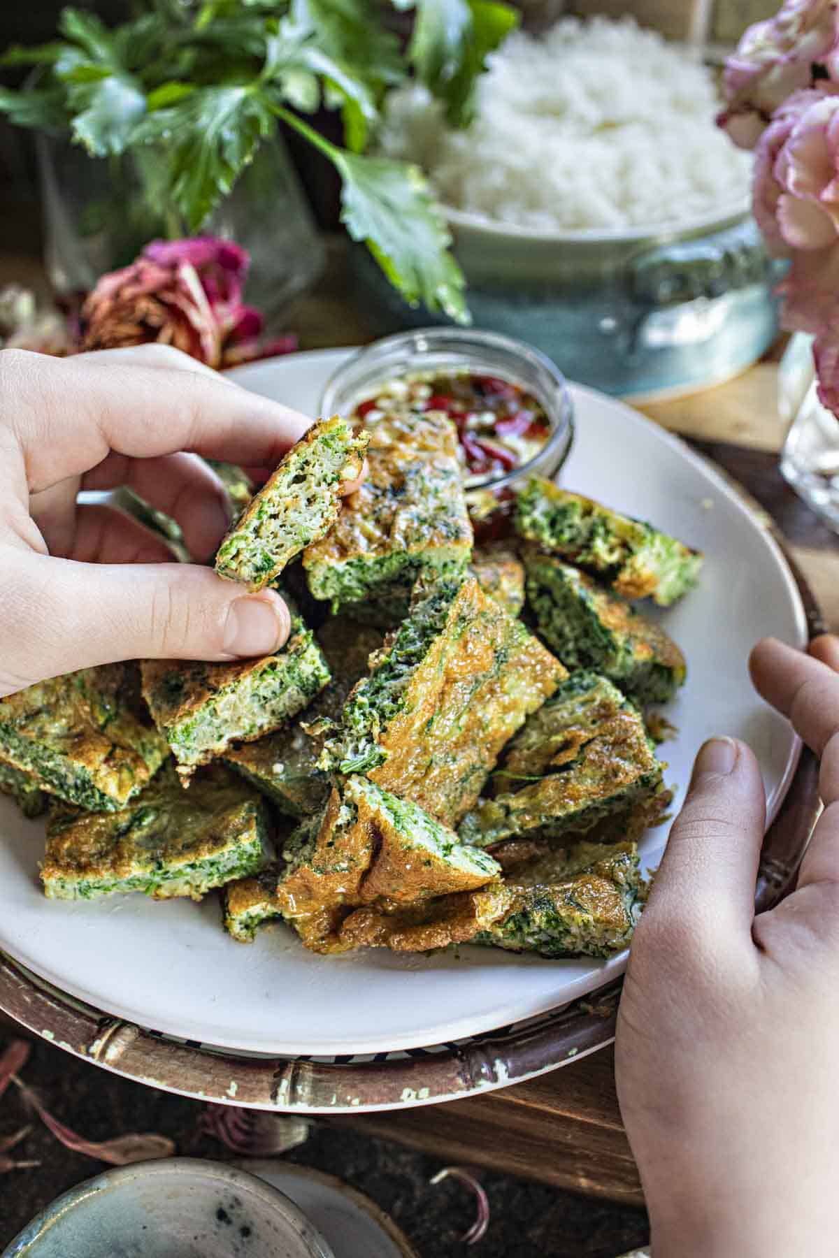 Hand holding a piece of Cha Om Thai omette patty. 