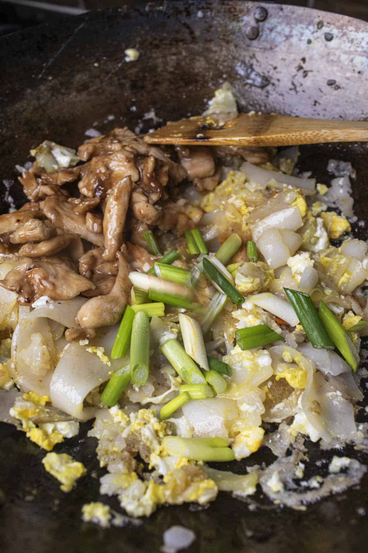 Thai chicken stir fry with wide noodles and green onions in a wok. 