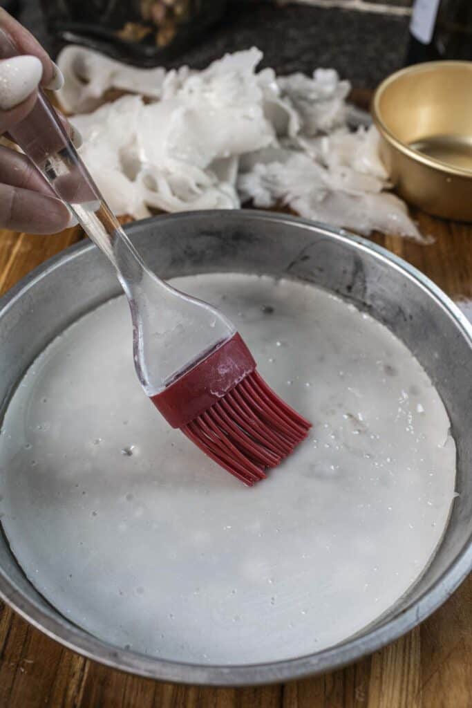 A brush with oil over steamed rice noodles in a baking pan.