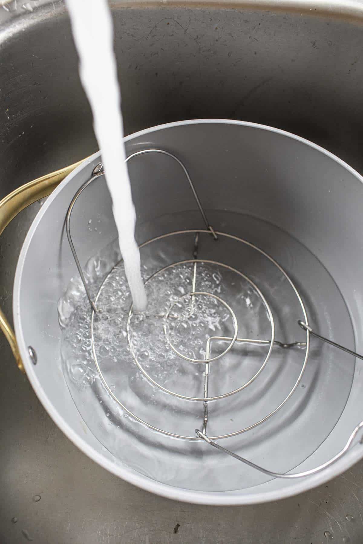 water from faucet pouring into pot with trivet in the bottom. 