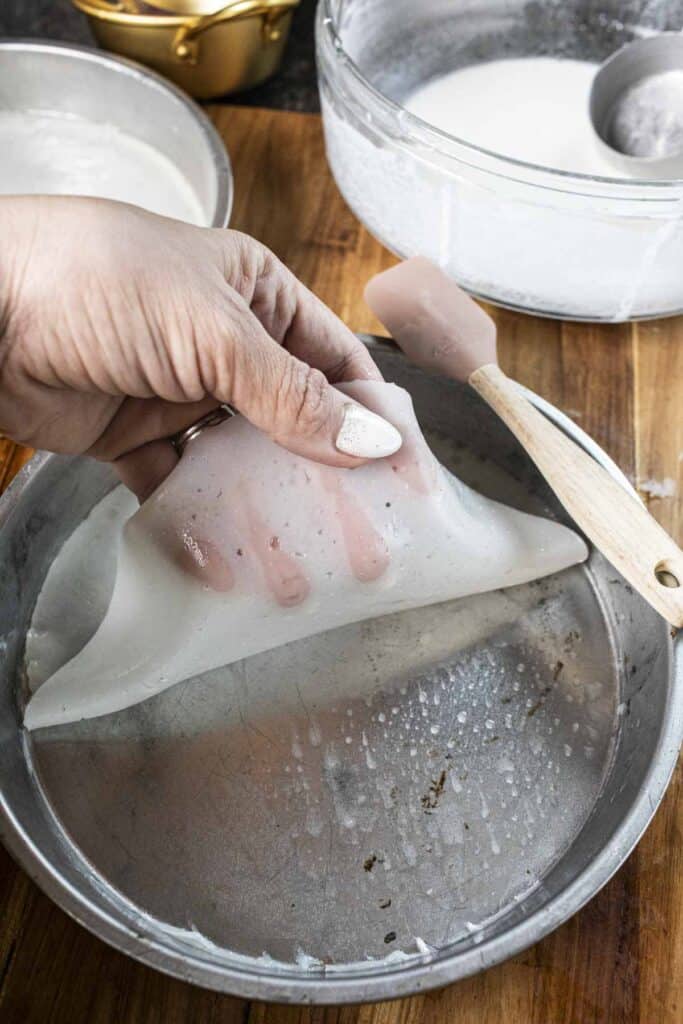 Fingers lifting cooked rice noodles in a baking pan.