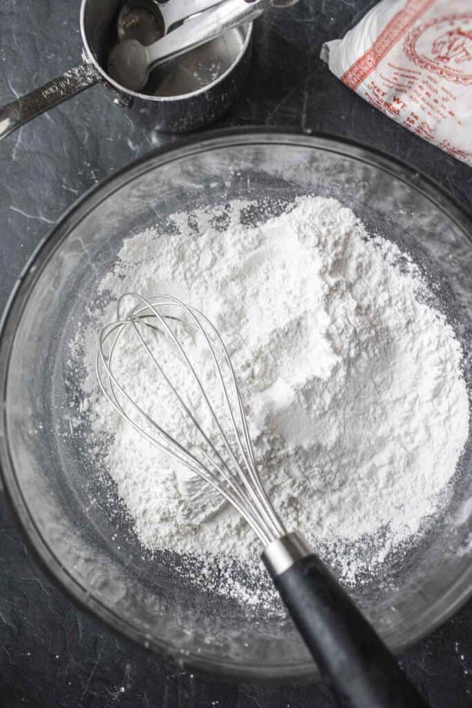 Flour and whisk in a glass bowl on the table. 