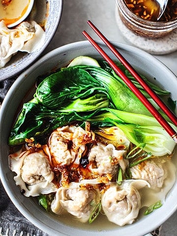 Thai wonton soup in a bowl with bok choy and chop sticks.