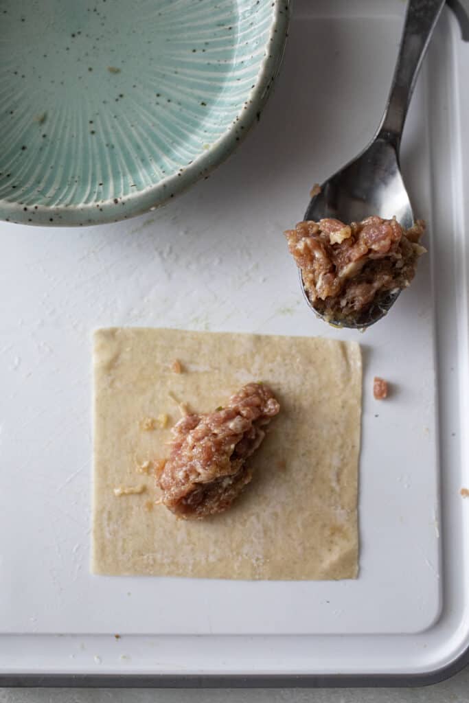 Pork filling on top of a wonton wrap with a spoon next to it. 