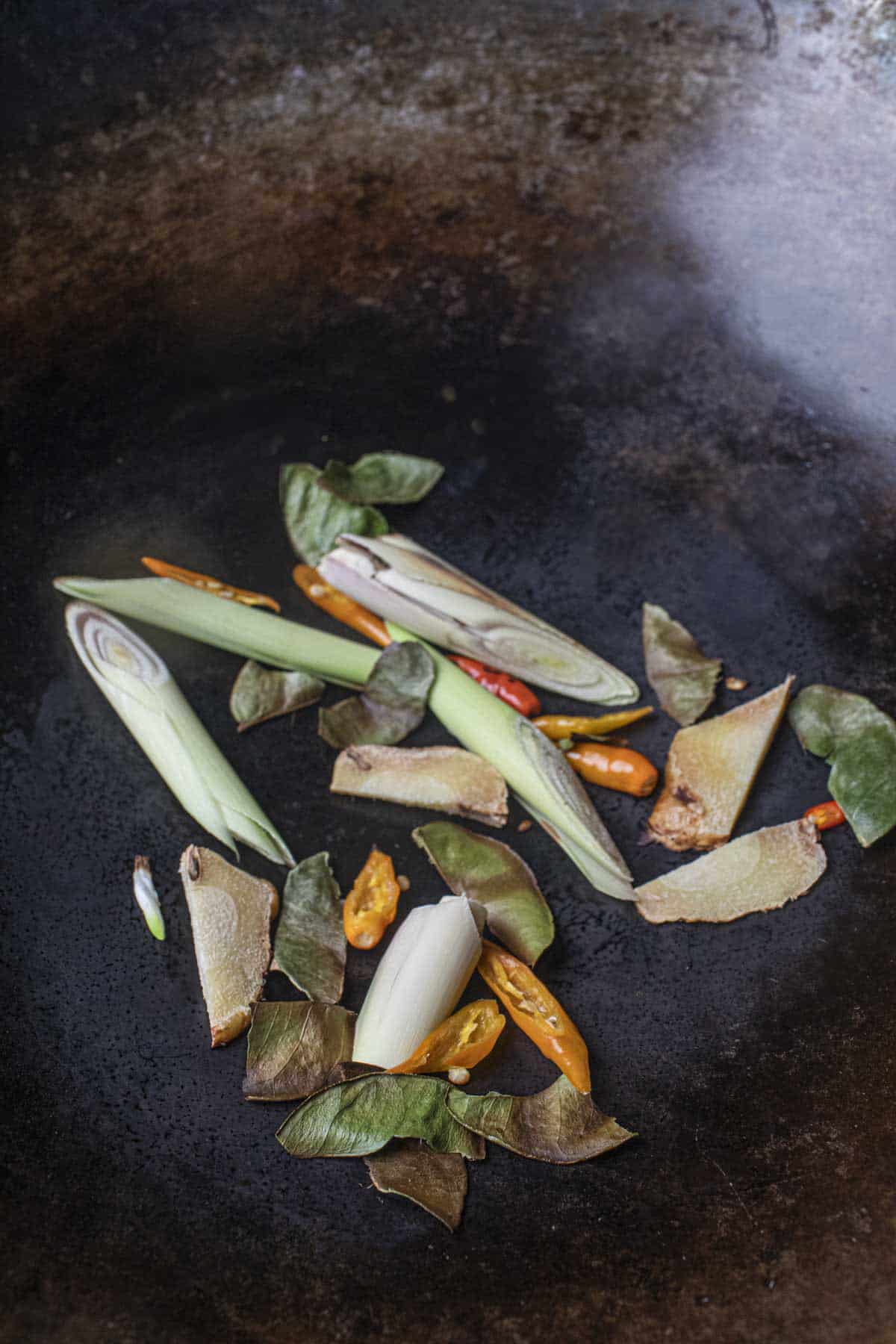 dry roasting galangal, lemongrass, kaffir lime leaves and Thai chilis in a wok. 