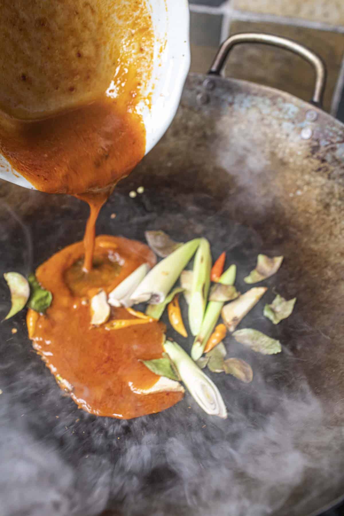 Tom Yum Sauce pouring into herbs In a wok. 