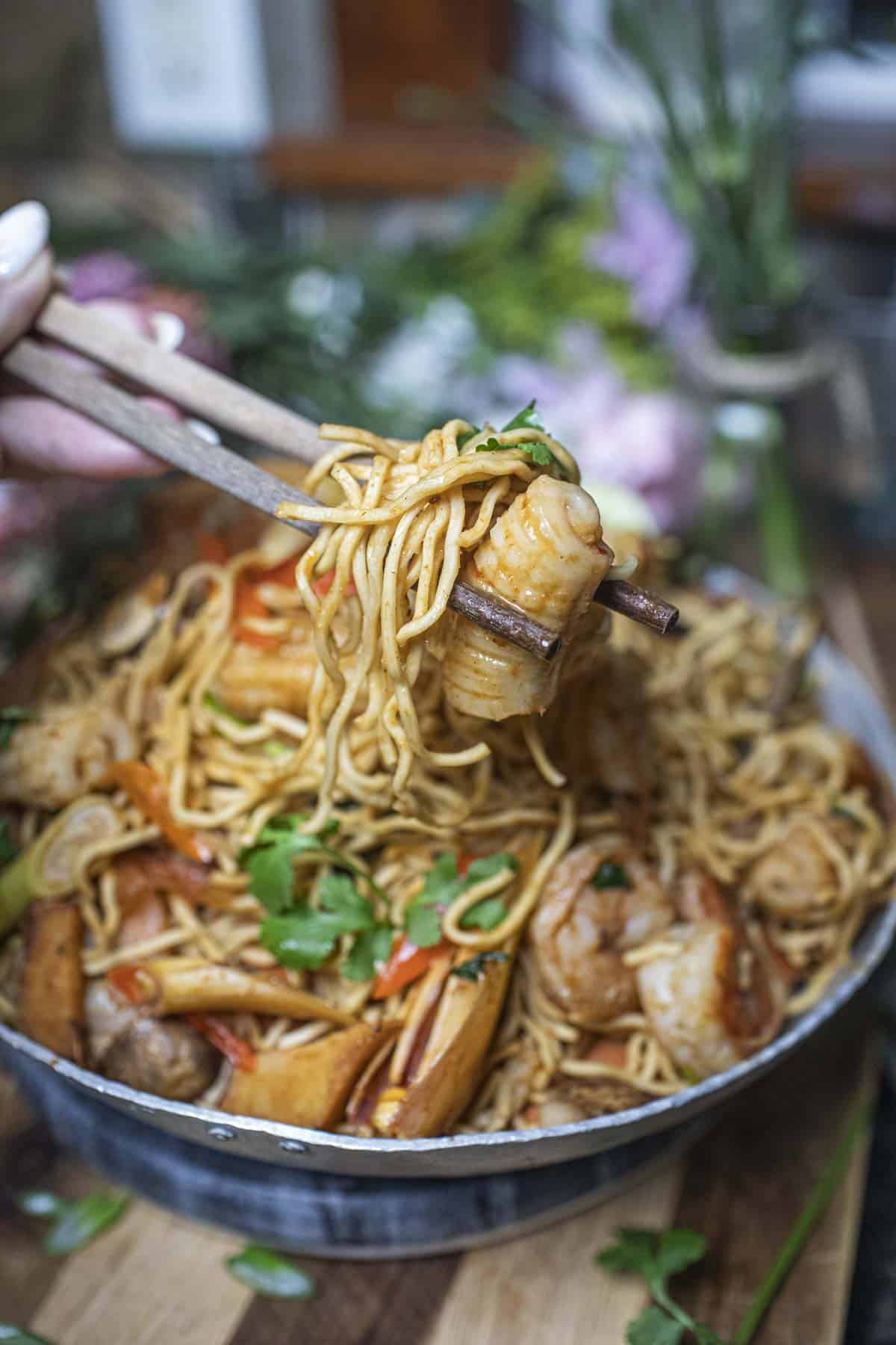 Chop sticks lifting Tom Yum fried noodles and squid from a bowl of Tom Yum noodles. 