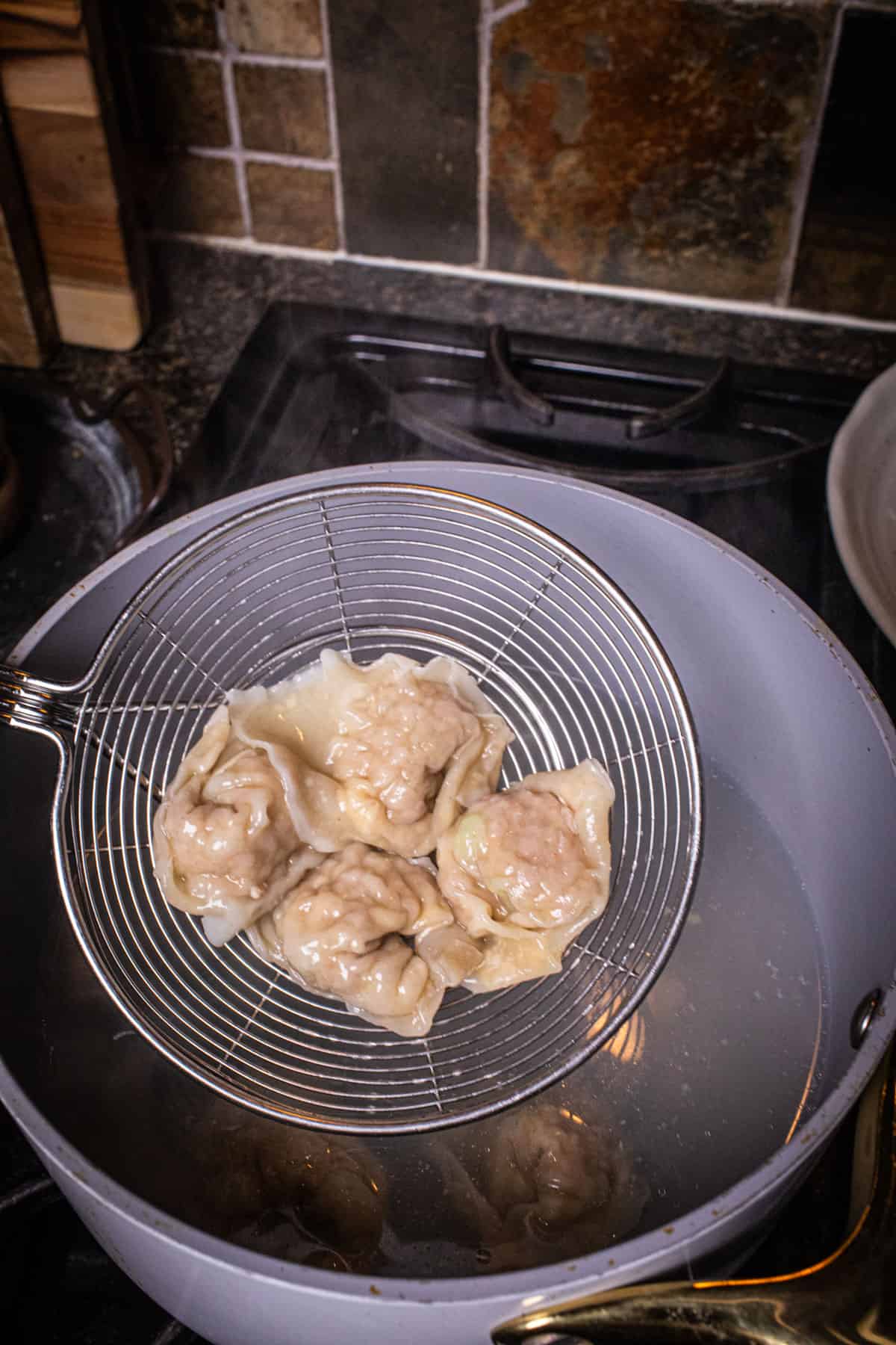 wire mesh lifting Wontons fro a pot of water. 