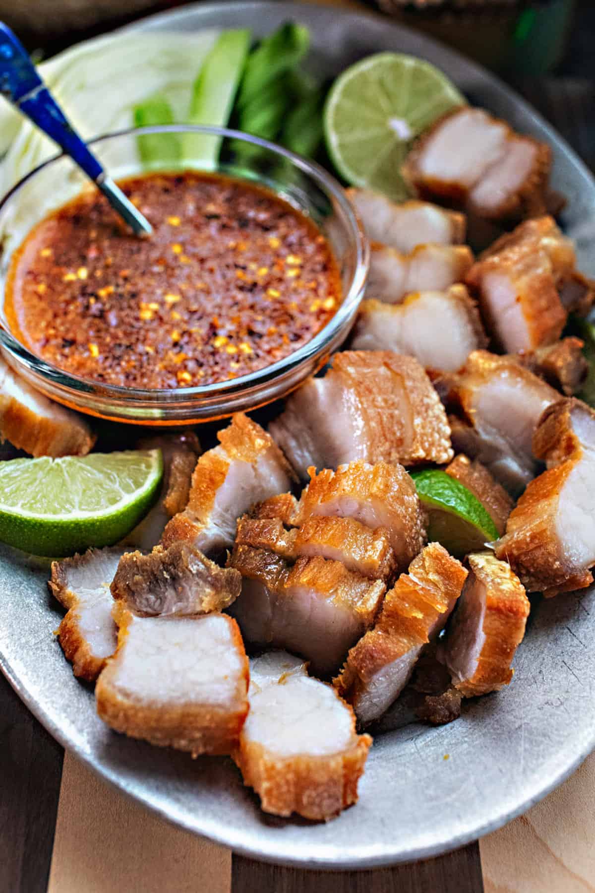 crispy pork belly slice on a plate with lime wedges and hot sauce. 