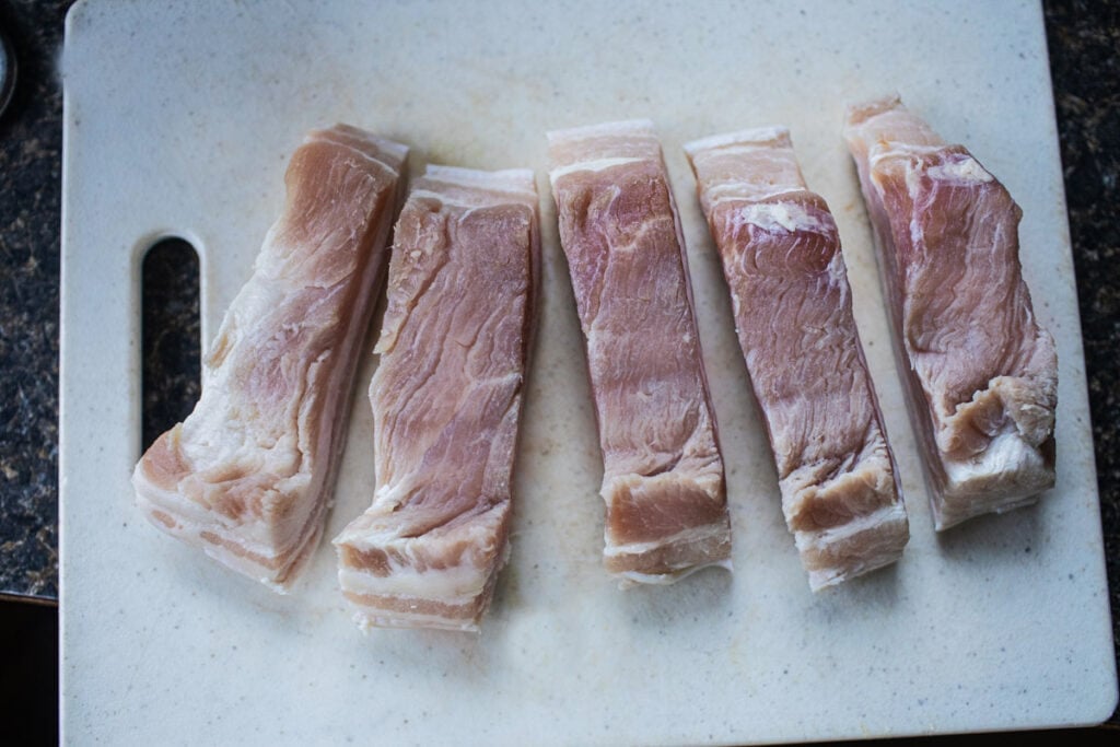 pork belly slices on a cutting board.