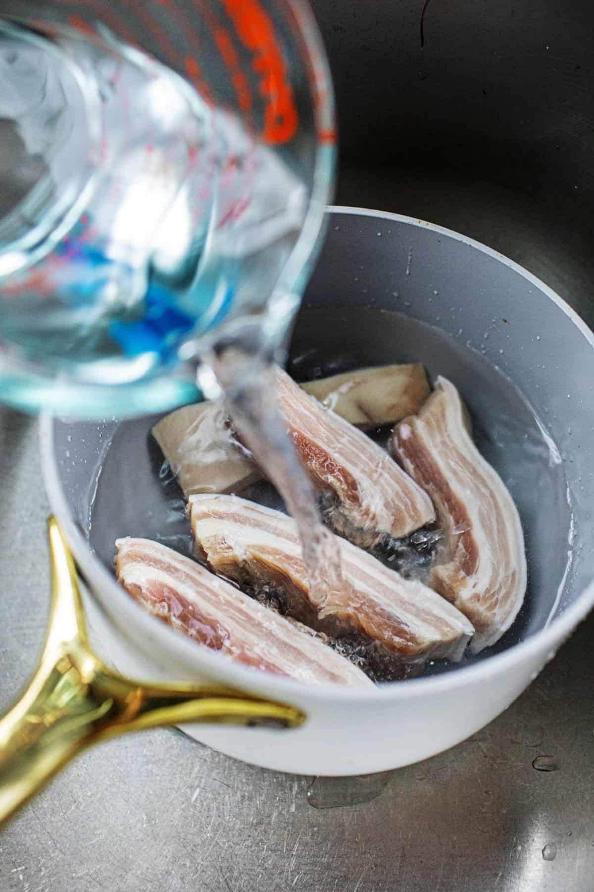 water pouring into Thai pork belly slices in a pot.