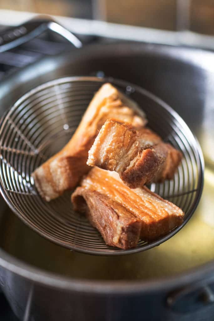 Wire mesh strainer lifting Fried pork slices from oil. 