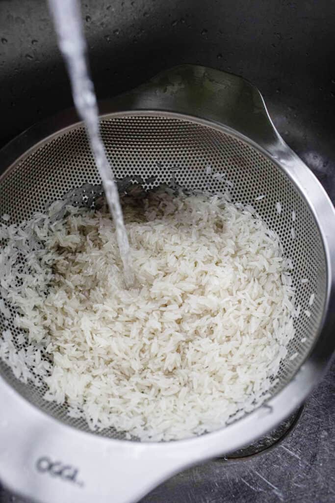 water pouring into raw rice in a colander. 
