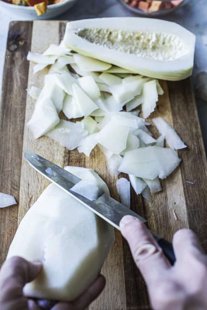 A hand slicing green papaya on a cutting board. 