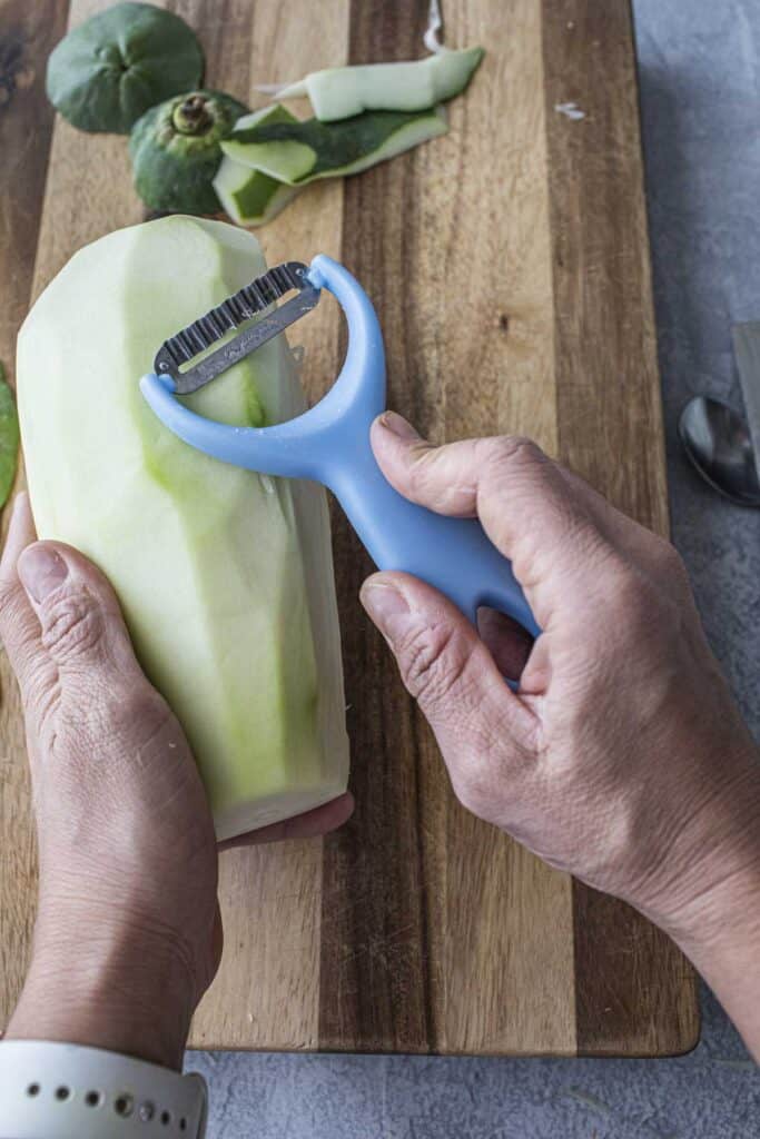 Hold holding a kiwi peeler over a peeled green papaya.