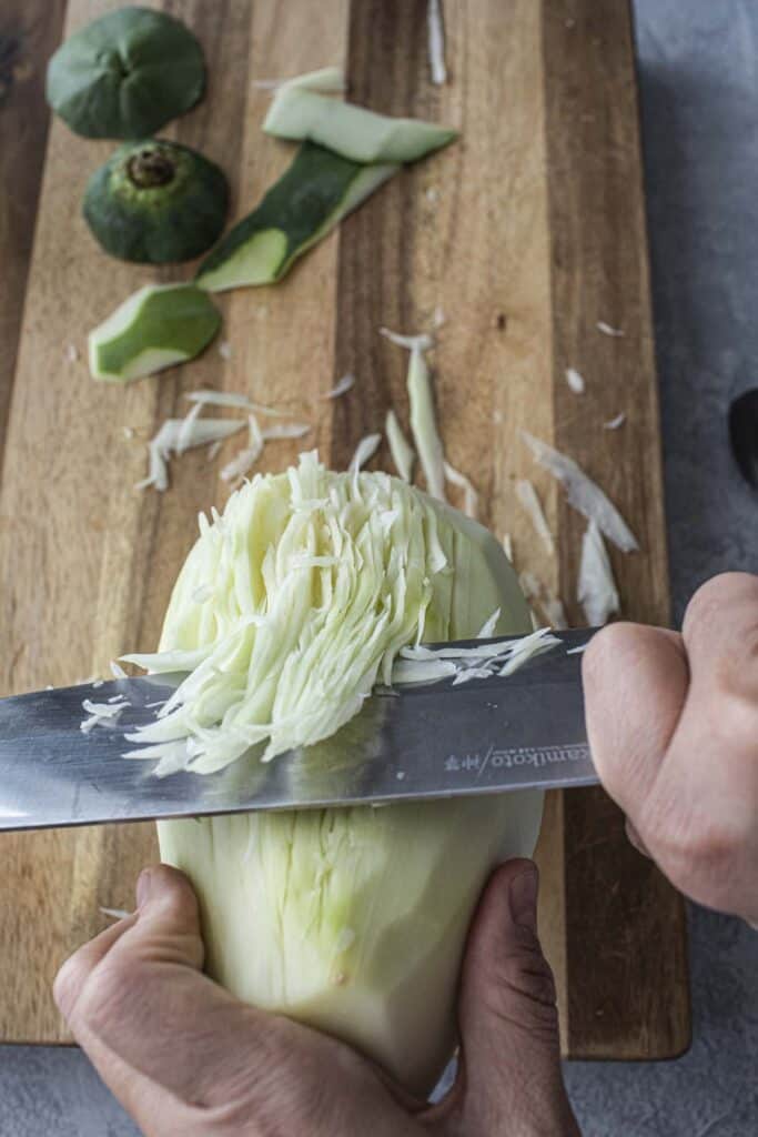 A knife cutting green papaya into shreds.