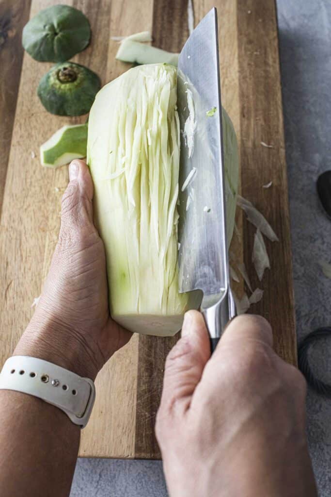 A hand Shredding young green papaya on a cutting board. 