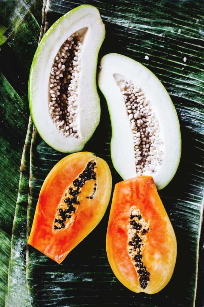 Green and ripe papayas cut in halves with seeds exposed.