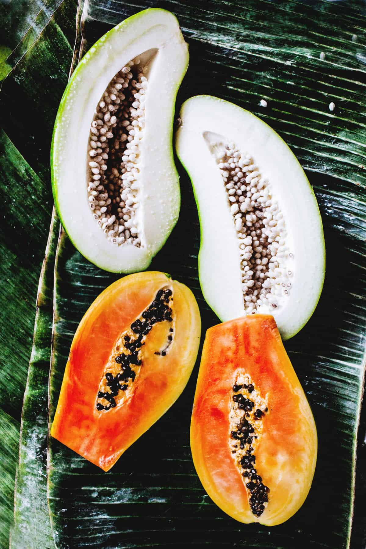 Green and orange papayas in halves on banana leaf. 