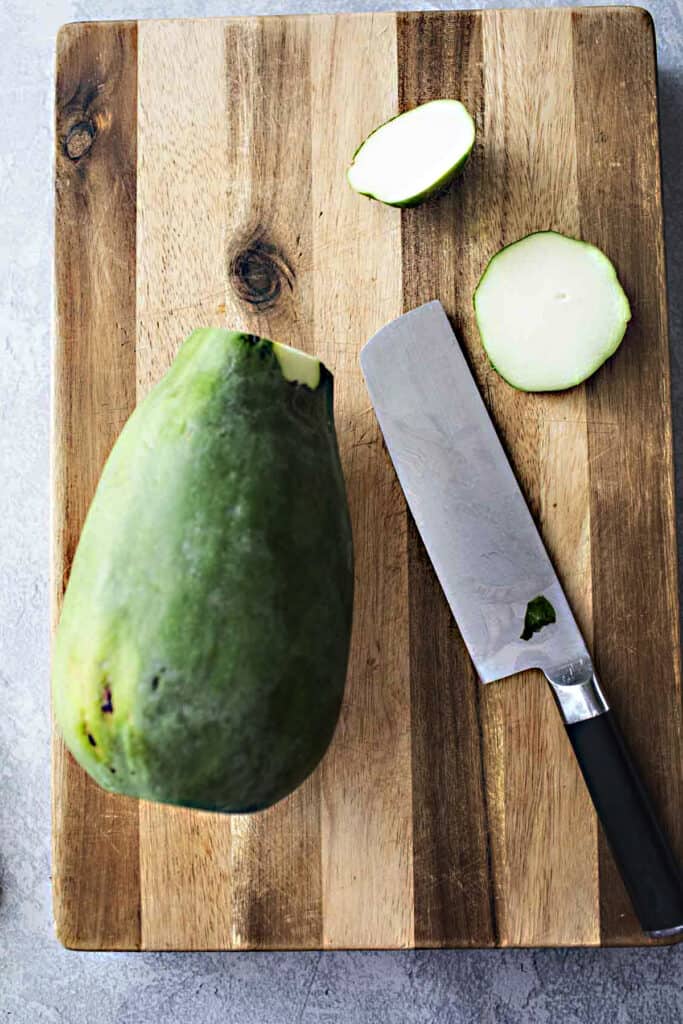 green papaya with tops peeled off on a cutting board with a knife.