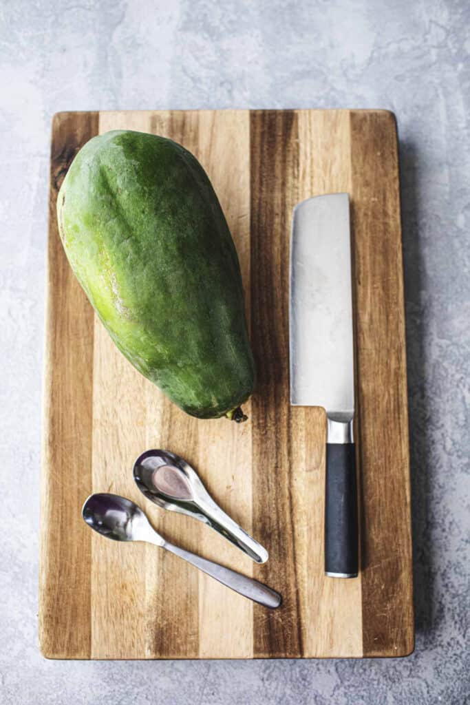 green papaya with a knife and spoons on a cutting board.