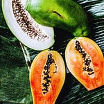 Ripe and green papaya in halves on a banana leaf.