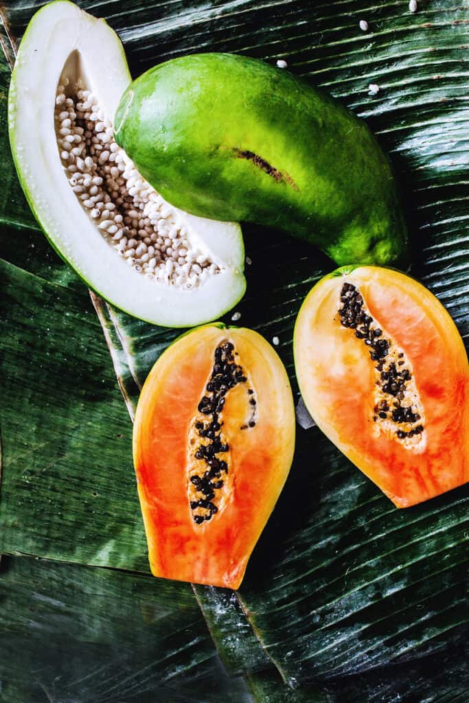 Ripe and green papaya in halves on a banana leaf.